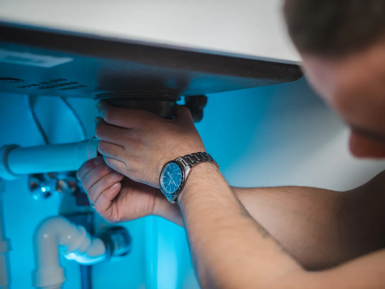 Close-up of a technician's hands inspecting pipework beneath a water heater
